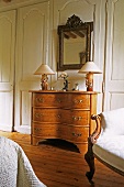 Table lamps on a Rococo chest of drawers with a mirror hanging above it in front of a wood panelled wall