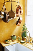 Gelbgetönte Küchenecke - gehängte Kupferpfannen und Spüle vor Fenster