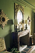 An elaborate mirror hung on a green wall above a mantelpiece