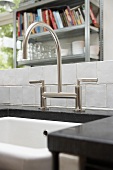 A designer tap on a washstand against a low wall with a view of a book shelf