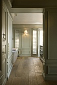 View through a doorway into a room with bright gray paneling, wall lighting and wood floor