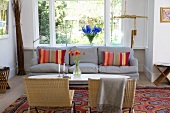 Wicker chairs and gray sofa around an oval coffee table in front of a floor to ceiling window