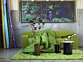 Flowers in vase and a black stool on a fluffy green rug in front of a green sofa with a quilt