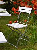 White folding chair in a garden with red flowers