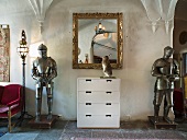 White cabinet with mirror in a gold frame between suits of armor in a castle