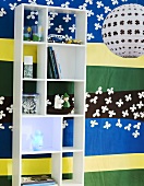White shelves in front of a colorful wall hanging and hanging lamp made of paper