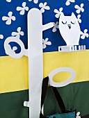 Child's coat rack made of white metal in front of a colorful wall hanging