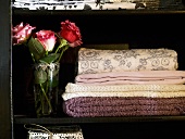 Quilted and embroidered wool blankets next to a bouquet of roses in a black cabinet