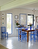 Open plan design dining room with white wood paneling and blue chairs at the dining table in front of a patio door