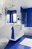 Washstand with mirror in a bathroom - white wood paneling on the wall and ceiling and blue mosaic tiles on the floor and wall around the bathtub