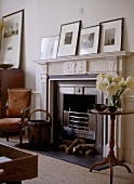 A detail of a traditional sitting room, showing carved fireplace with black hearth, wooden round side table