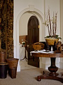 A traditional hallway with an arched doorway, door open, wooden round pedestal table, wicker baskets