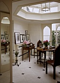 A modern dining room with tiled walls and skylight, a round wood table, chairs with gothic style backs, tiled floor