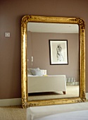 Large gold painted framed mirror against brown wall reflecting bed