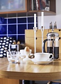 A detail of a modern kitchen, wood breakfast table, cup and saucer, coffee, caffetiere, boiled egg, candlesticks, candles,