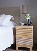 A detail of a modern bedroom, double bed with upholstered headboard, lamp, bedside table, flowers, vase, clock,