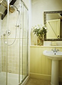 Yellow bathroom with shower cubicle and an arrangement of lilies above a washbasin.