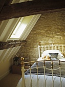 Brass bed with teddy bears under a pitched attic roof and skylight.