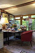 A home office space inside a shed with a wooden desk and a red chair upholstered chair on wooden floorboards.