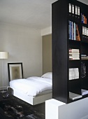 A single bed behind a partition of book shelves