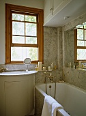 Waschbecken mit Unterschrank vor Fenster neben Badewanne im Bad mit Steinfliesen