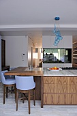 Blue bar stools at island unit breakfast bar with wooden drawers in contemporary kitchen