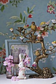 A candelabra, animal figurines and glasses against a wall with floral patterned wallpaper
