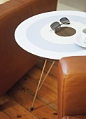 A detail of a modern sitting room, a round painted table, set between leather armchairs, wooden floor,