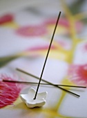 Incense sticks and star shaped holder on floral patterned tablecloth.