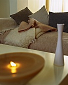 Vase and burning candle on a table in front of a couch with cushions