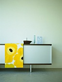 Sideboard im Retro-Stil und Tischläufer mit gelbem Blumenmuster vor blauer Wand