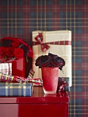 A detail of a red vase with roses, wrapped presents, set on a red cabinet,