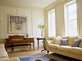 Sofa vor Fenster und antikes Klavier im weiss getäfeltem Wohnraum