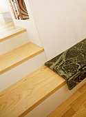 A detail of wooden steps, white walls, books on shelf, marble step,