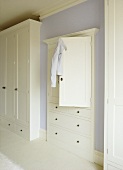 A detail of a pale blue bedroom with painted white, fitted wardrobes, cupboard and drawer unit,