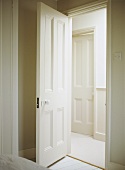 A view through an open, painted panelled interior door into a neutral hallway