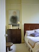 View through open door to bedroom with upholstered headboard and cushions on bed.