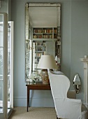 A detail of a traditional sitting room, upholstered wing back armchair, Venetian mirror, side table