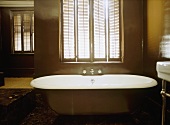 A detail of a traditional, bathroom, a free standing roll top bath, window shutters