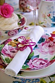 A rolled napkin with a ring and a floral patterned place setting