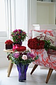 Various bunches of flowers in coloured glass vases next to a 1950s style armchair