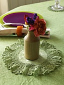 Kleiner Blumenstrauss in Keramikvase auf Häkeldecke und farbiges Gedeck