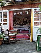 Wood house with terrace and rocking chair in front of an open door looking into a bedroom