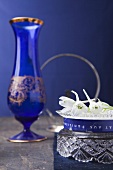 White delphiniums in a bowl and a blue vase against a blue wall