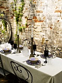 A table in front of a brick wall laid with black wine glasses and candles
