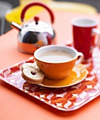 A cup of coffee with a jam biscuit on a tray