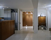 A modern open-plan living room with a kitchen counter and an antique cupboard next to an open door