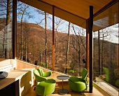 Grüne Designersessel in Wohnraumecke vor verglaster Fassade mit Aussicht