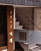 Outdoor concrete steps and a bridge with metal banisters next to a wooden sign with Japanese characters