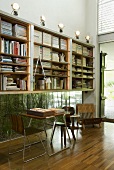 A study corner with a non-matching table and chair in front of a bookshelf above a floor-level window